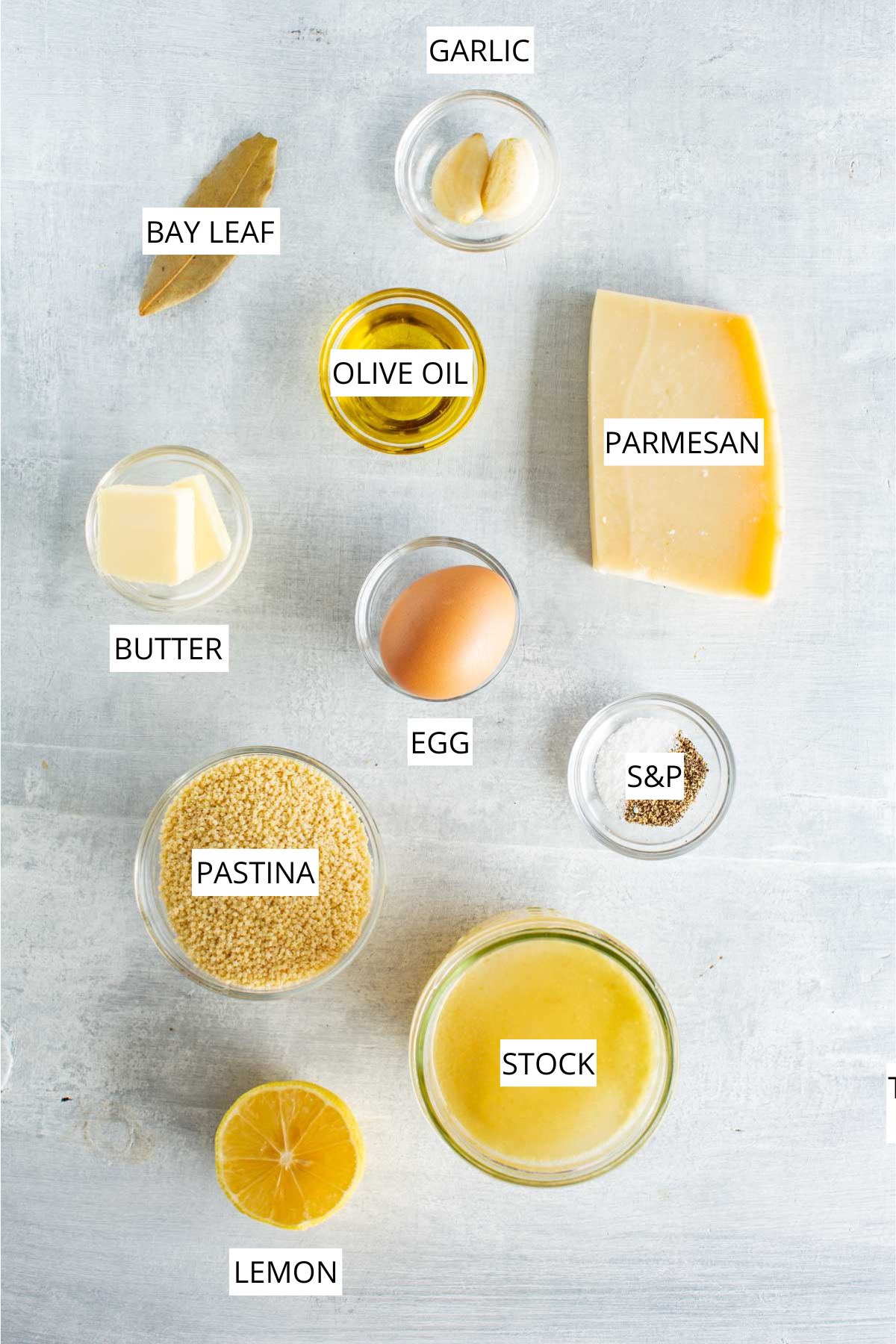 Labeled overhead layout of ingredients for pastina including stock, pastina, egg, butter, garlic cloves, Parmesan, olive oil, lemon and a bay leaf on a light background.