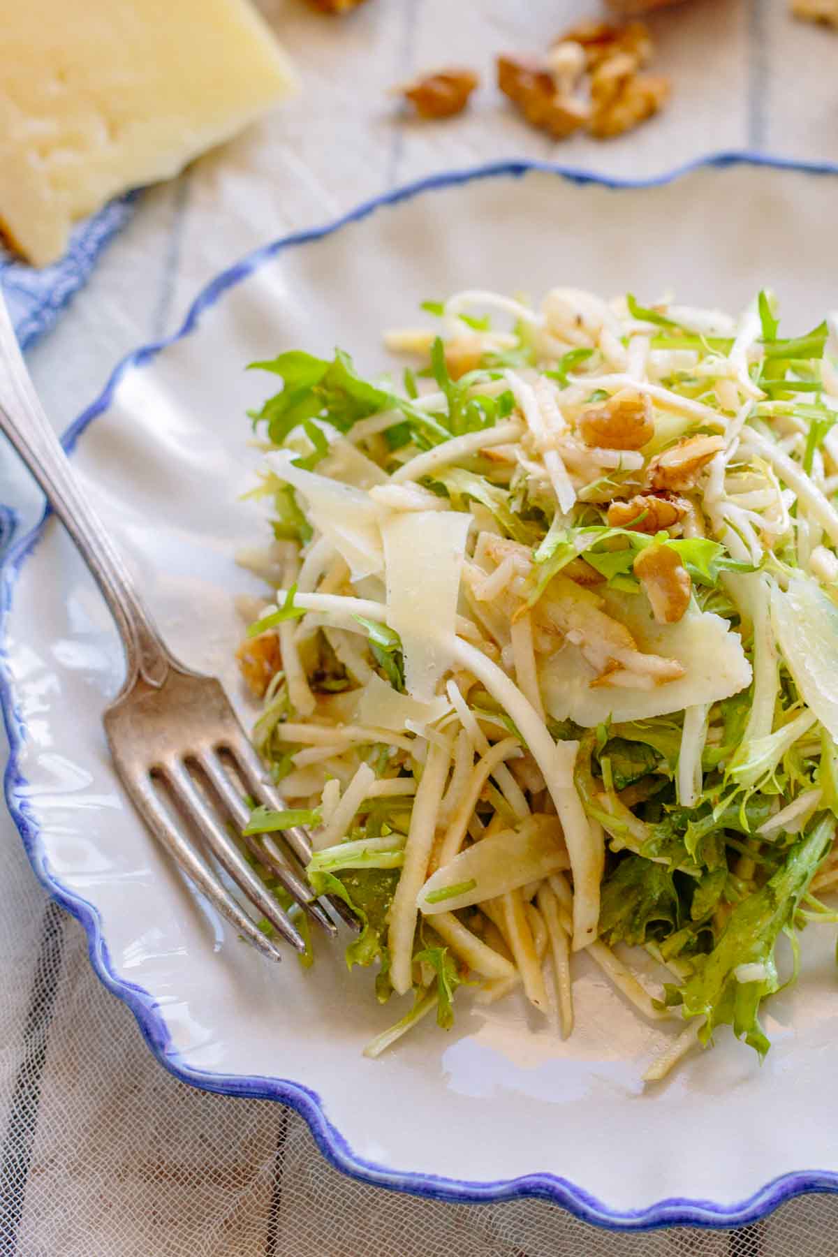 Thinly shaved celery root and pear tossed with frisee, walnuts and manchego on a white plate with a fork.