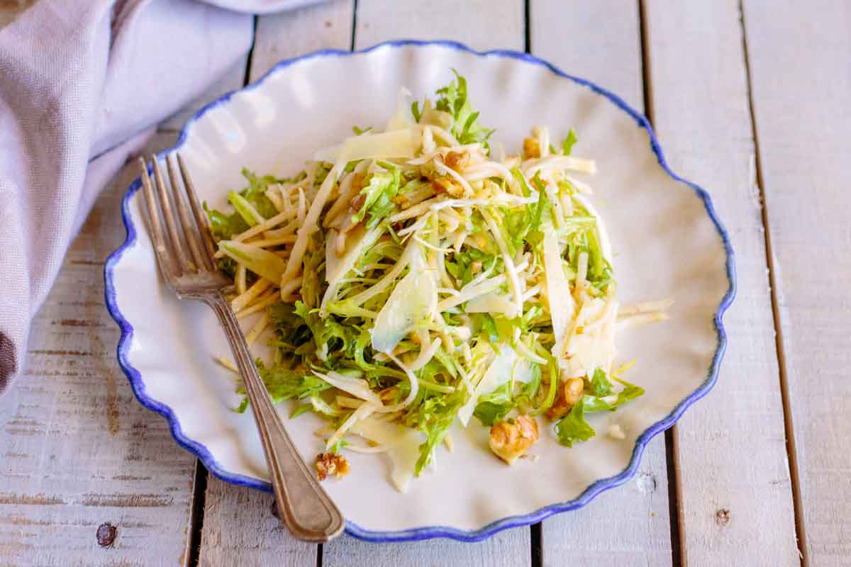 A wider view of the celery root and pear salad on a scalloped white plate with a fork resting on the side.