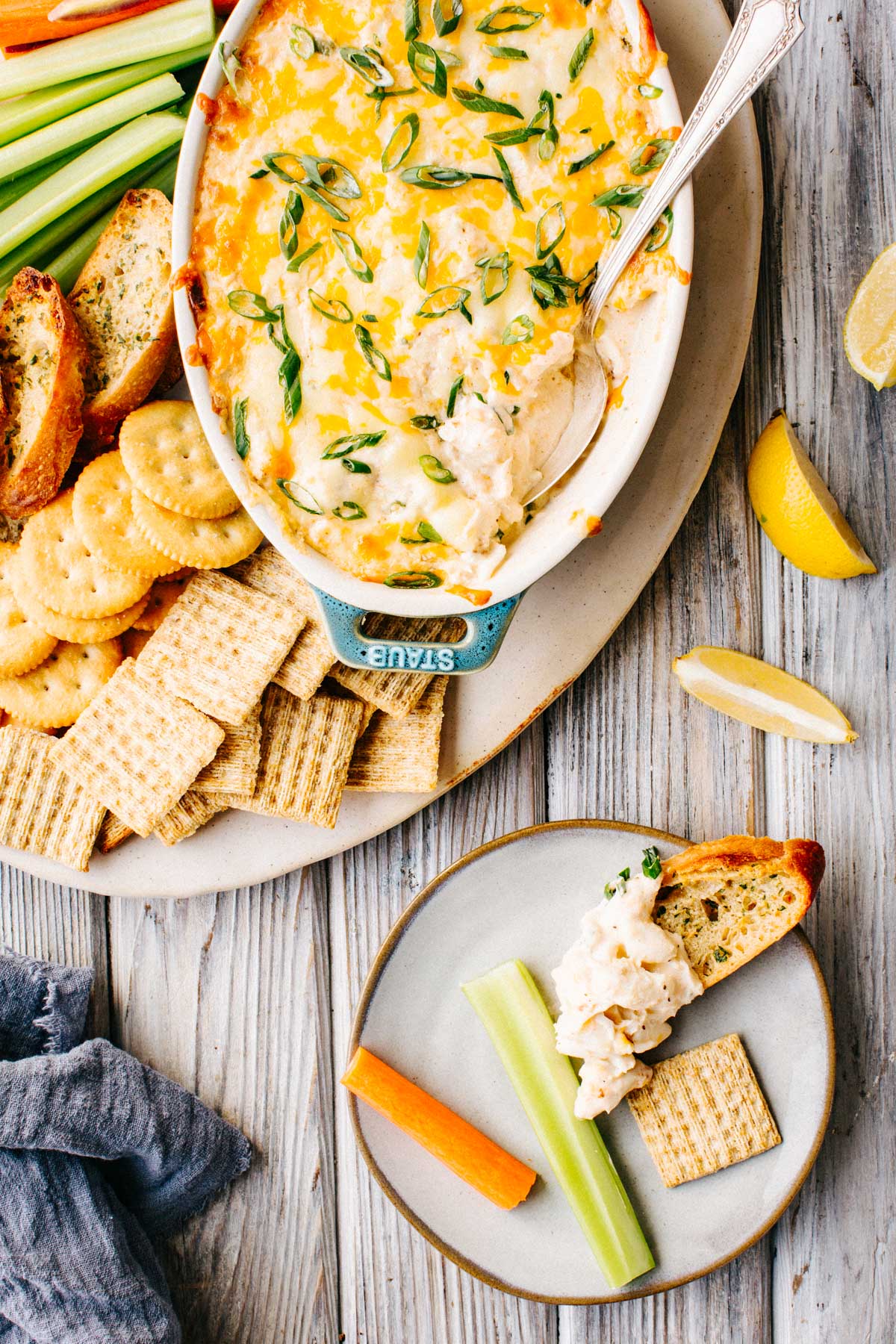 A small plate with a dollop of crab dip on crostini alongside a celery stick, carrot stick and cracker.