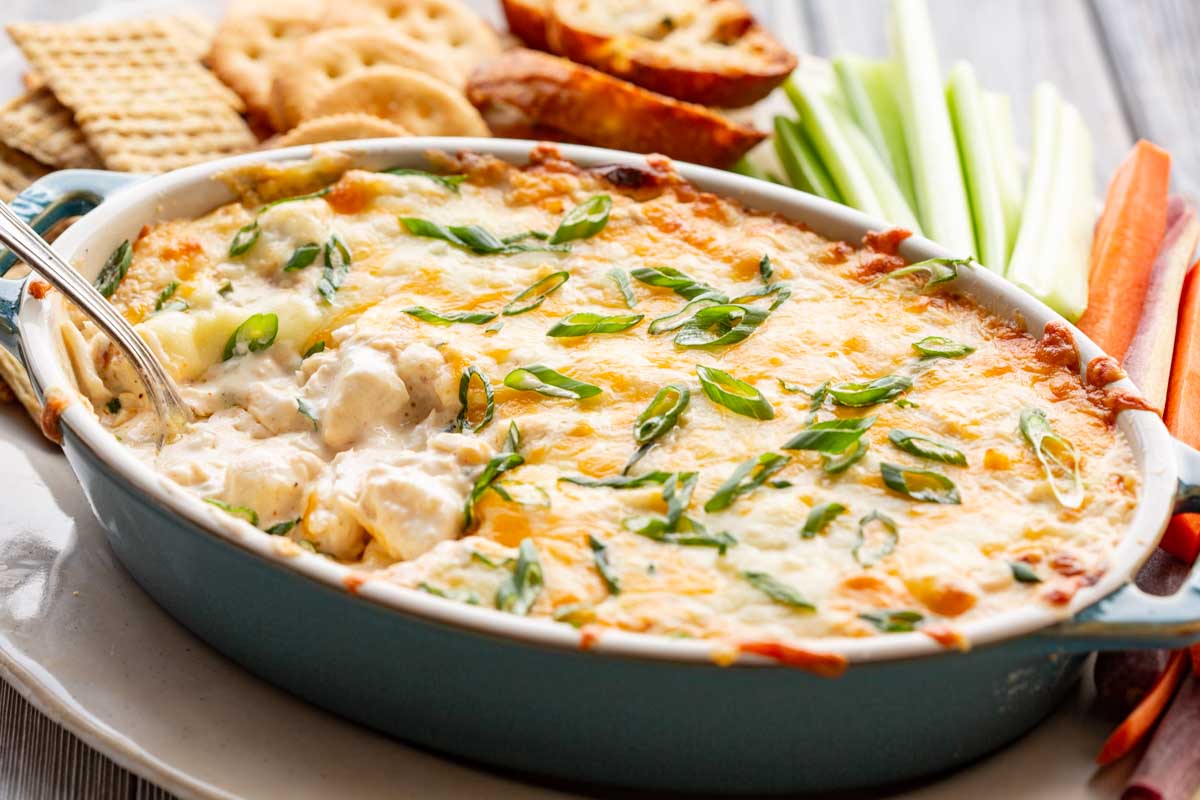 A close up of creamy baked crab dip with chunks of crabmeat under a layer of melted cheese and scallions.