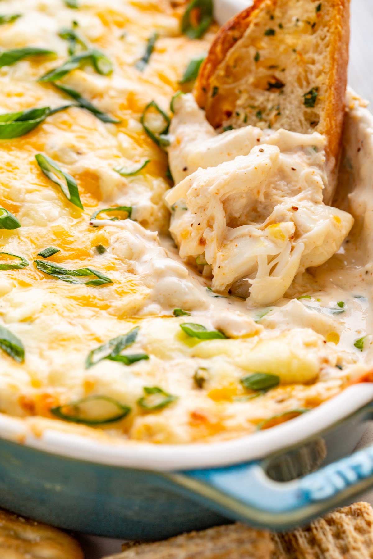 A piece of toasted bread lifting a scoop of creamy crab dip with visible chunks of lump crabmeat.