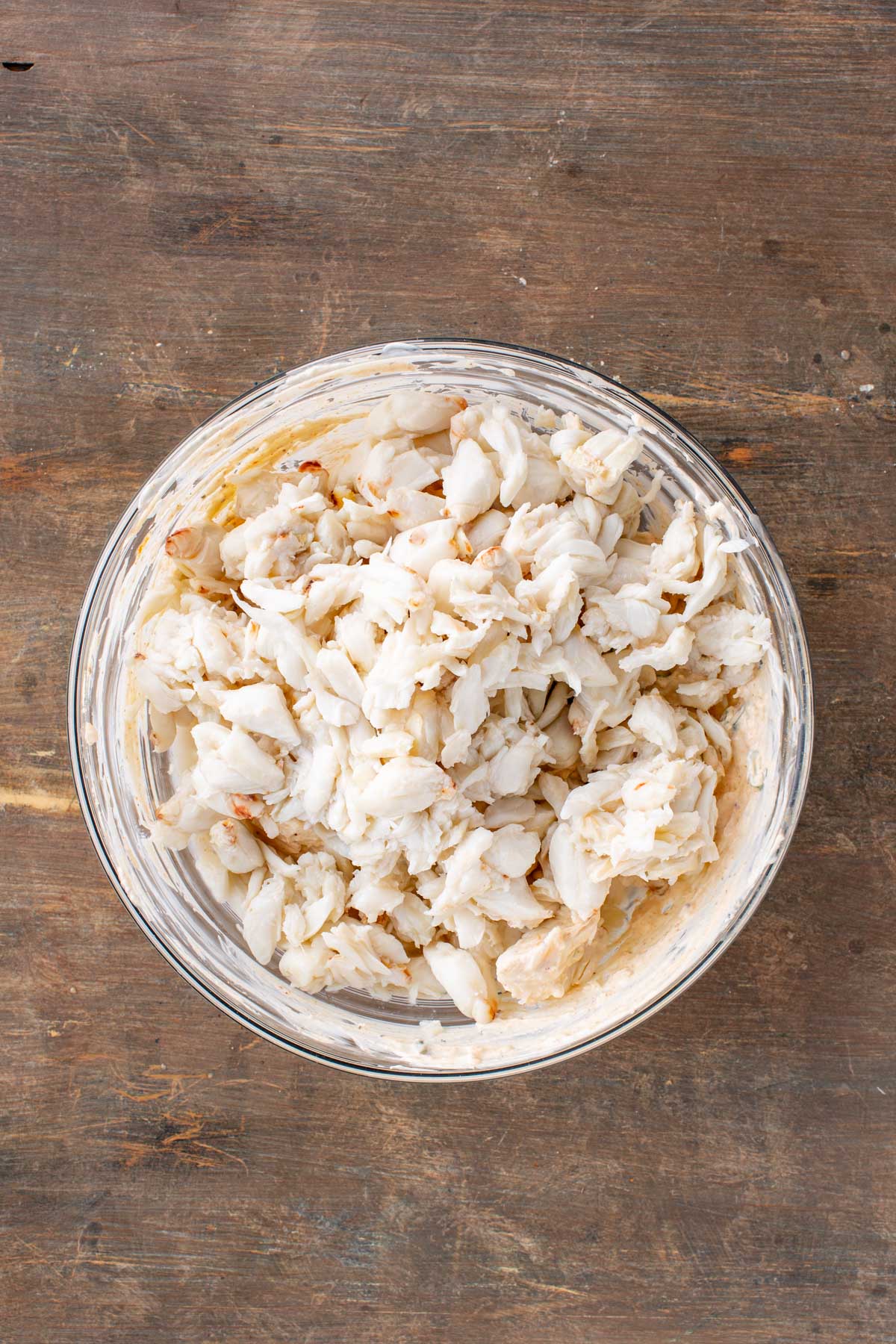 A mound of lump crabmeat resting on top of the seasoned cheese mixture in a glass bowl.