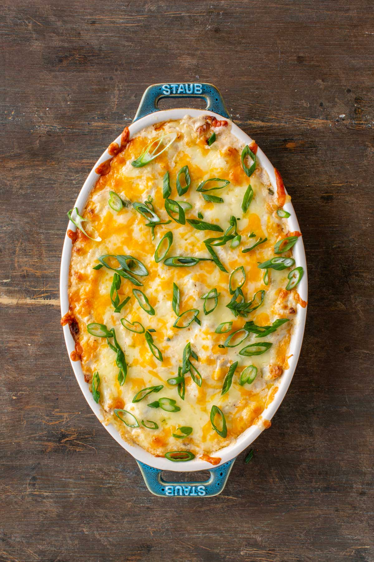 A hot bubbling crab dip topped with melted cheese and sliced scallions in an oval baking dish.