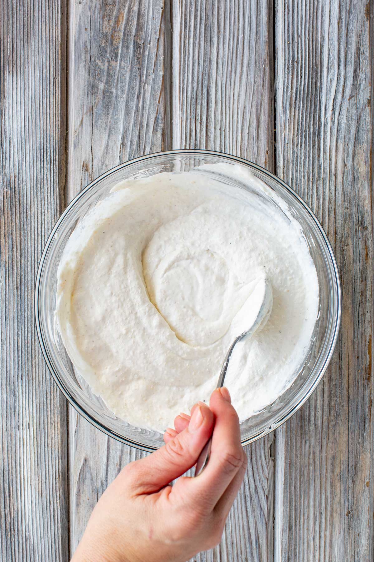 Hand holding a spoon and mixing the creamy horseradish sauce in a glass bowl until smooth.