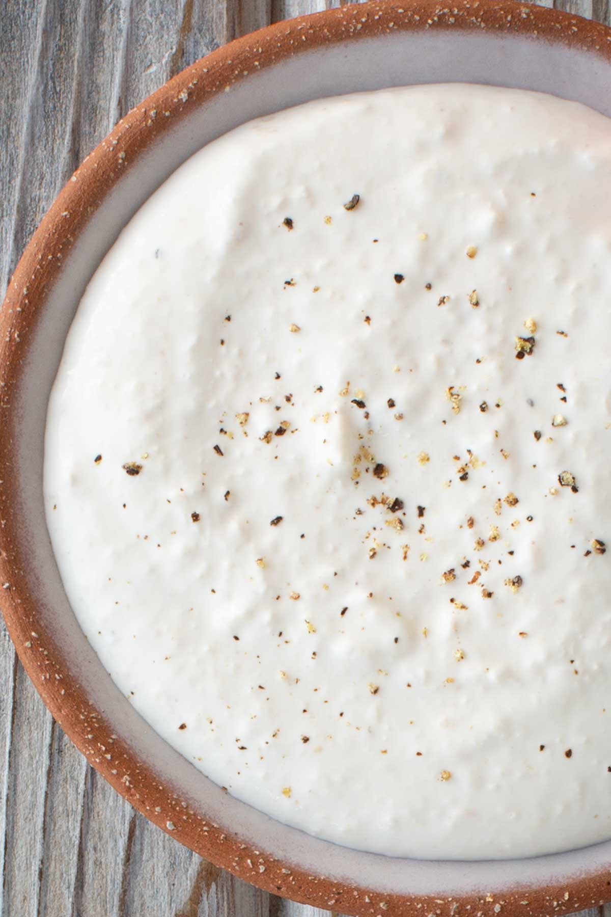 A close view of creamy horseradish sauce in a bowl with cracked pepper sprinkled over the top.