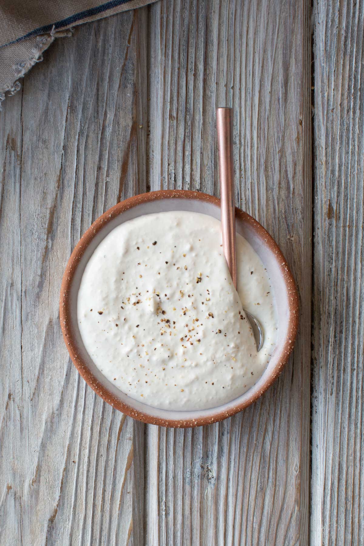 A terracotta bowl filled with creamy horseradish sauce, garnished with pepper, with a spoon resting in the bowl.