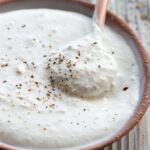 A spoon lifting a dollop of thick horseradish sauce from a small bowl, showing its creamy texture.