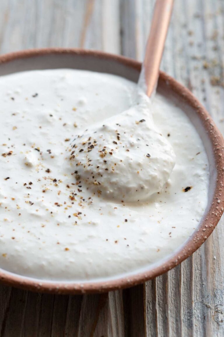 A spoon lifting a dollop of thick horseradish sauce from a small bowl, showing its creamy texture.