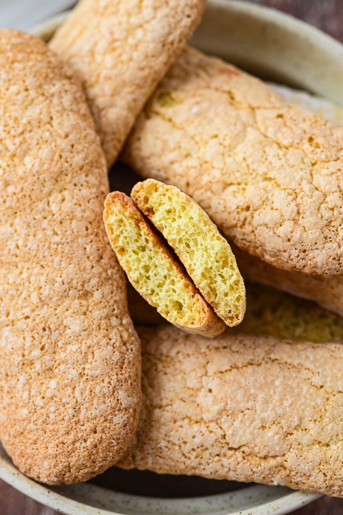 A ladyfinger broken in half to show its airy, sponge-like interior surrounded by more cookies.