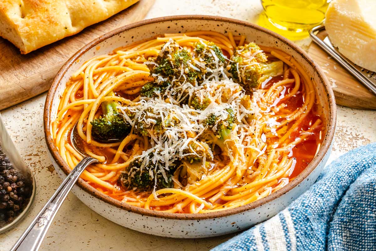 Close-up view of Sicilian broccoli soup showing spaghetti strands, broccoli florets, tomato broth, and grated cheese.