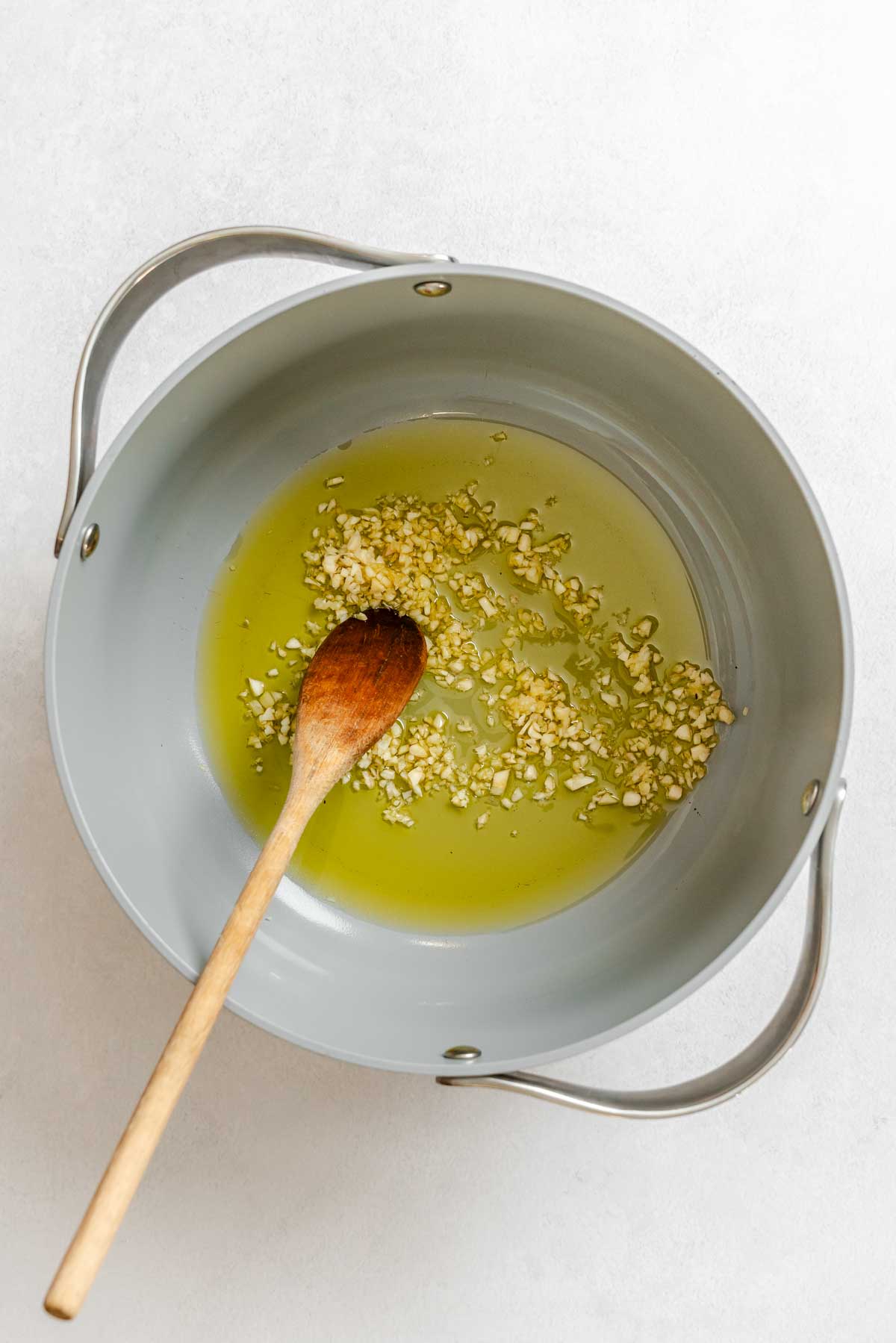 Minced garlic gently cooking in olive oil in a large pot with a wooden spoon.