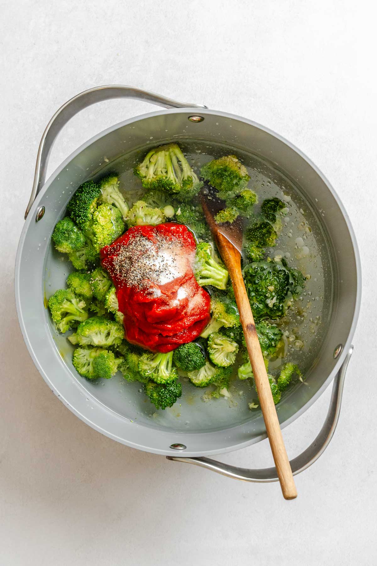 Broccoli florets, tomato paste, salt and black pepper added to the pot with garlic and olive oil before simmering.
