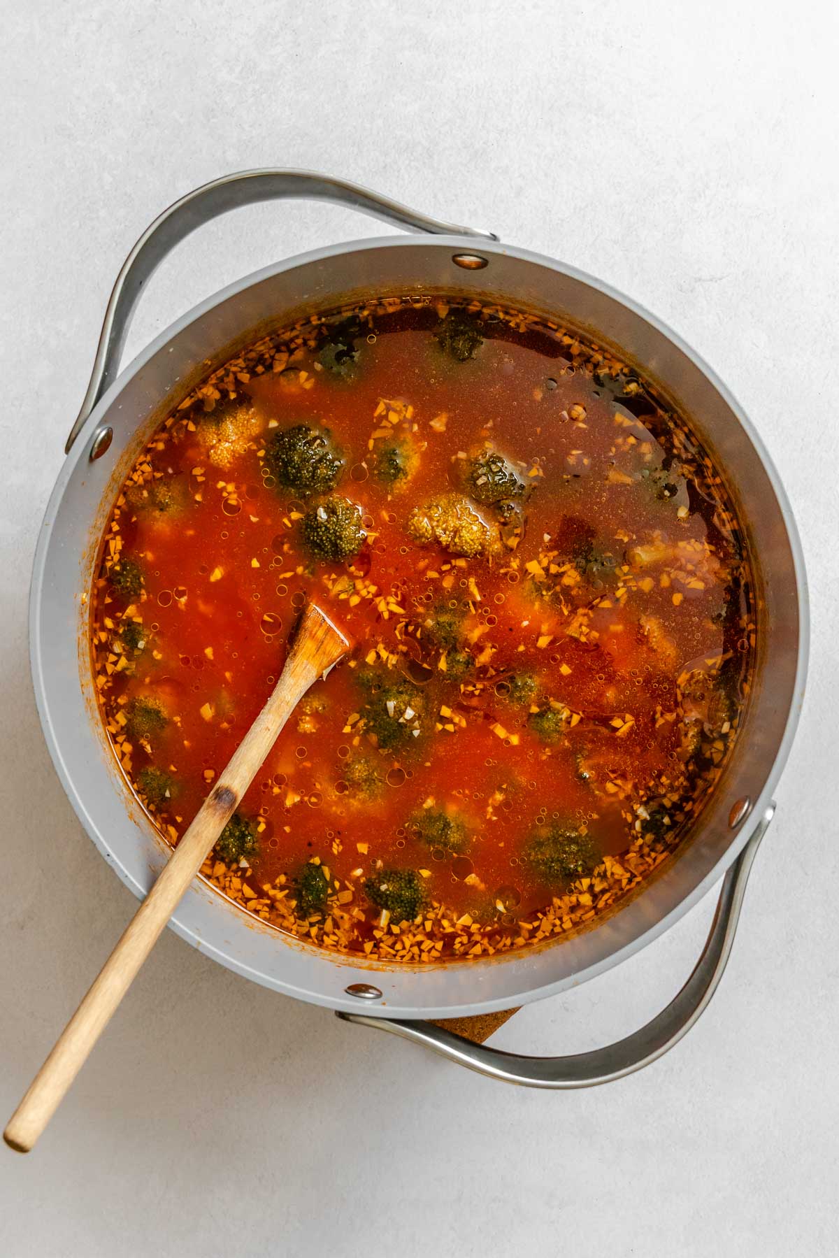 Broccoli soup simmering in a pot with tomato broth, tender florets, and bits of garlic floating throughout.