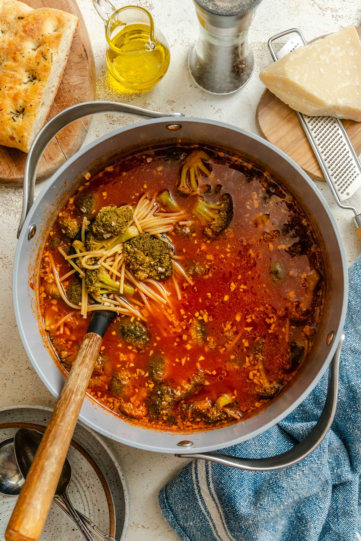 Cooked spaghetti and broccoli stirred together in the tomato-based soup inside the pot.