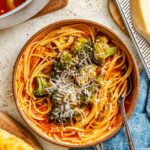 Finished Sicilian broccoli soup with pasta and broccoli ready to serve, with olive oil, bread, and cheese nearby.