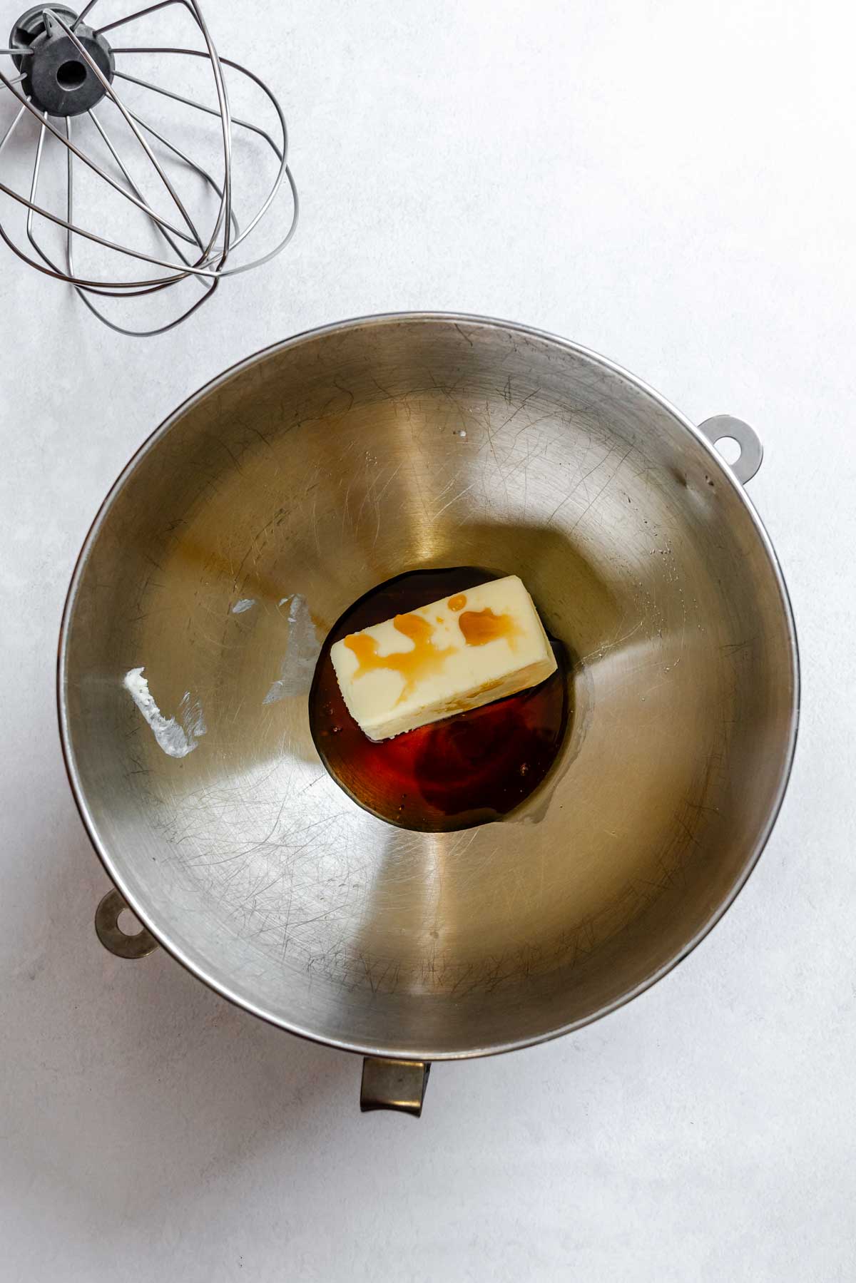 Softened butter and maple syrup added together in a metal stand mixer bowl before whipping.