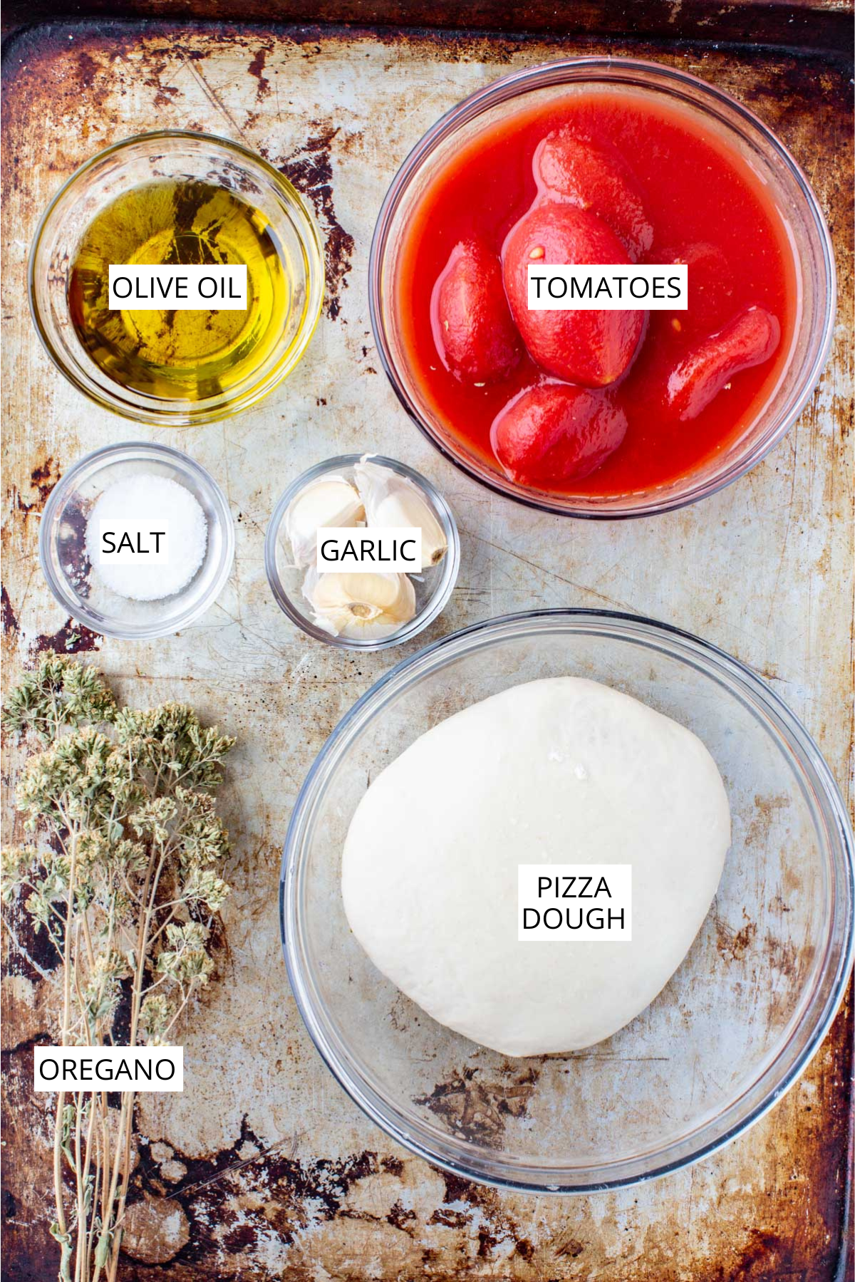 Ingredients for Neapolitan pizza marinara including pizza dough, canned peeled tomatoes, olive oil, garlic, salt and dried oregano arranged on a sheet pan.