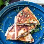Golden brown apple butter quesadilla wedges stacked on a blue ceramic plate, finished with chopped fresh cilantro.