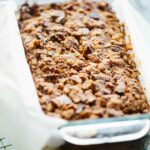 Whole pecan streusel banana bread resting in a parchment-lined loaf pan, showcasing the golden brown streusel crust.