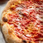 Tight close-up of Neapolitan pizza marinara highlighting the soft dough, blistered edges and chunky tomato sauce.