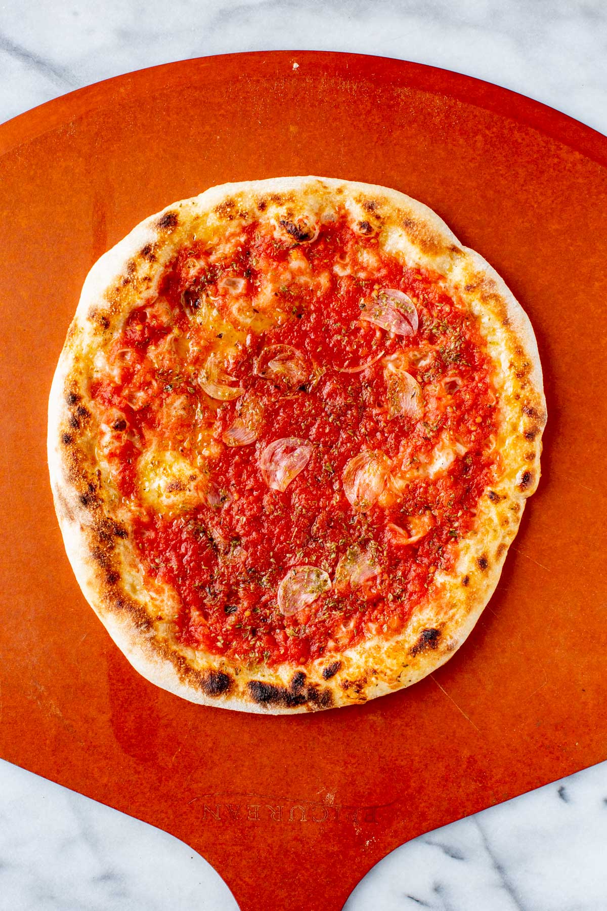 Baked Neapolitan pizza marinara with a blistered crust and tomato sauce resting on a wooden pizza peel over marble.