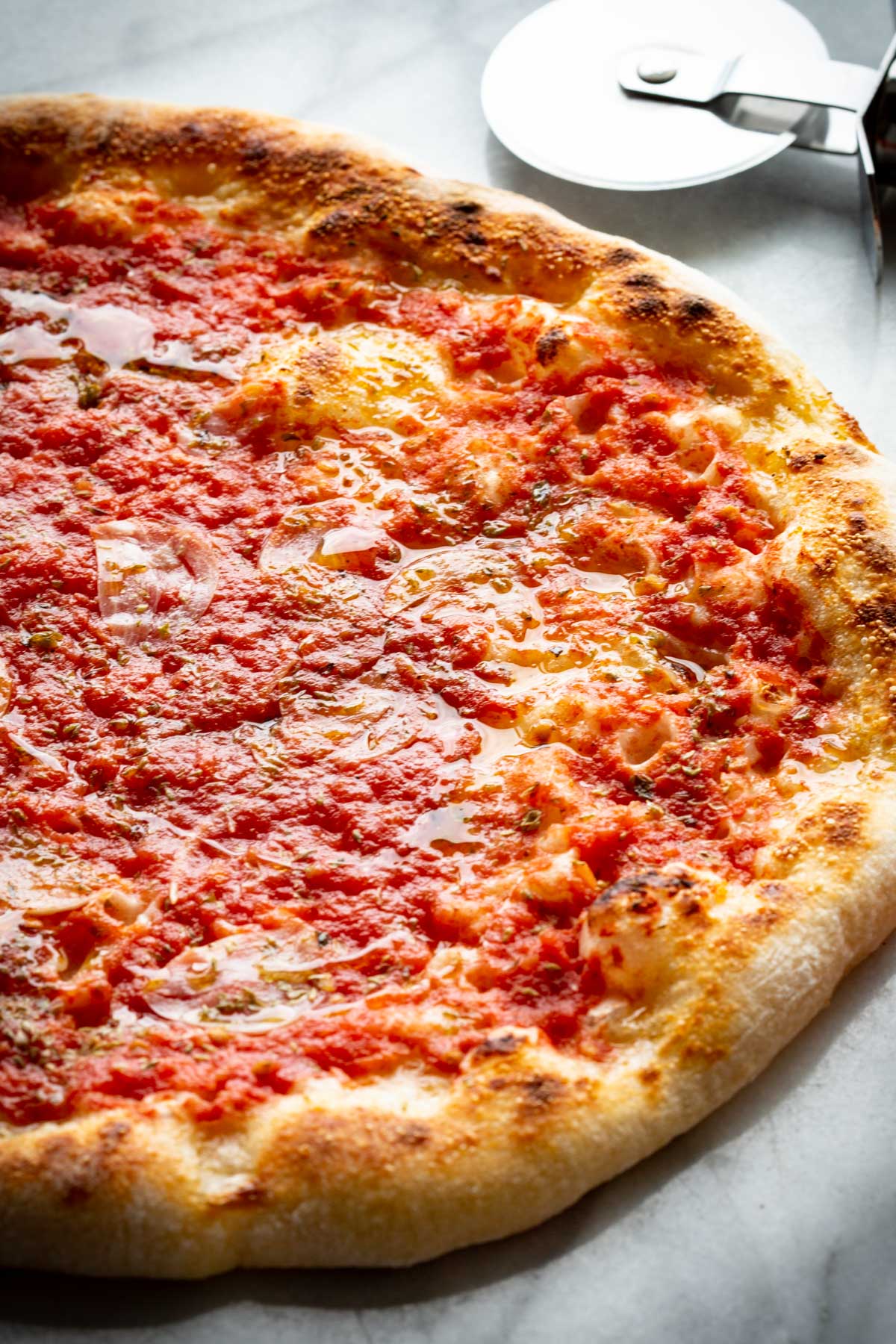 Close-up of Neapolitan pizza marinara showing airy, charred crust and rustic tomato sauce glistening with olive oil.