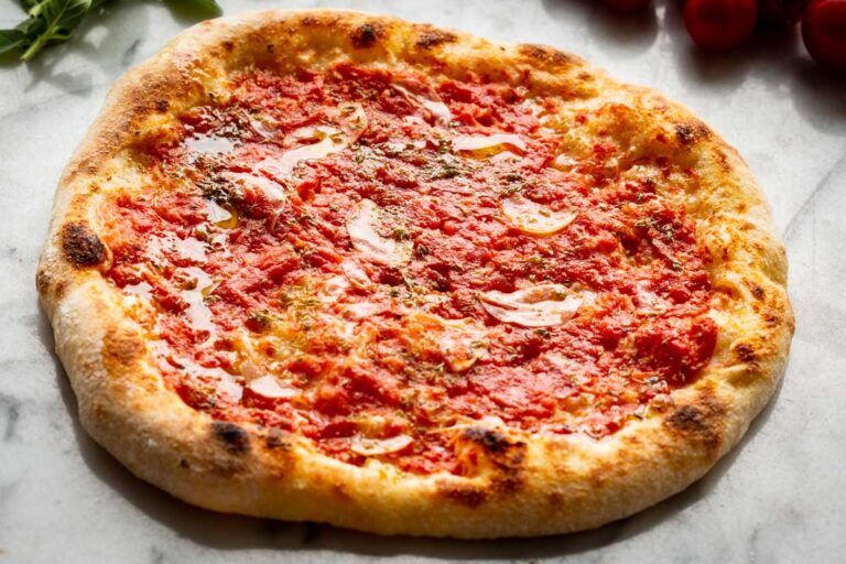 Whole Neapolitan pizza marinara with puffy, leopard-spotted crust and evenly spread tomato sauce on a marble countertop.