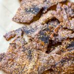 Thin, rustic quinoa crackers broken into irregular pieces on parchment paper, baked until dark golden and crisp with seeded topping.