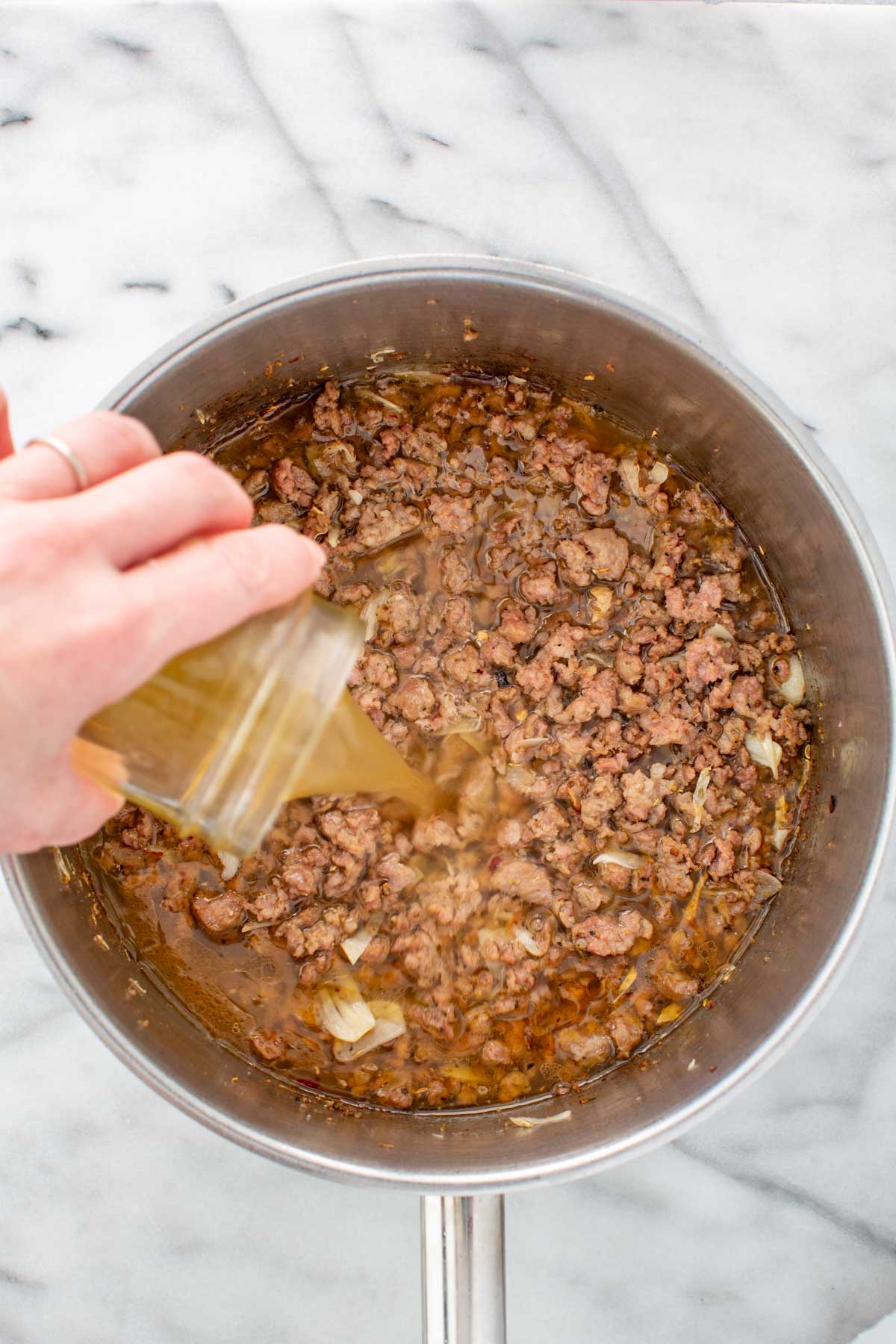 Chicken stock being poured into the pot to deglaze the browned sausage, garlic, and spices.