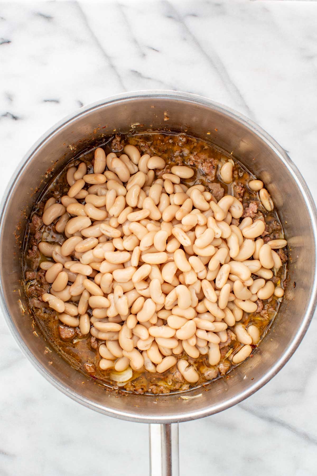 Cannellini beans added to the pot with sausage and broth, ready to simmer.