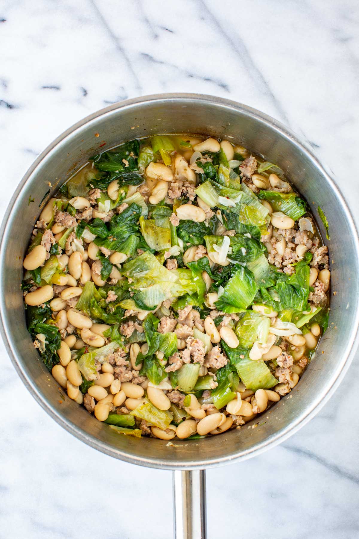 The stew simmering with wilted escarole, sausage, and white beans in a light, savory broth.