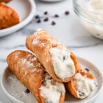 Crispy cannoli shell filled with creamy ricotta and chocolate chips, dusted with powdered sugar.
