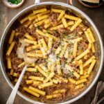 Ziti pasta tossed with slow cooked beef and onion Genovese sauce, topped with grated cheese and parsley in a skillet.