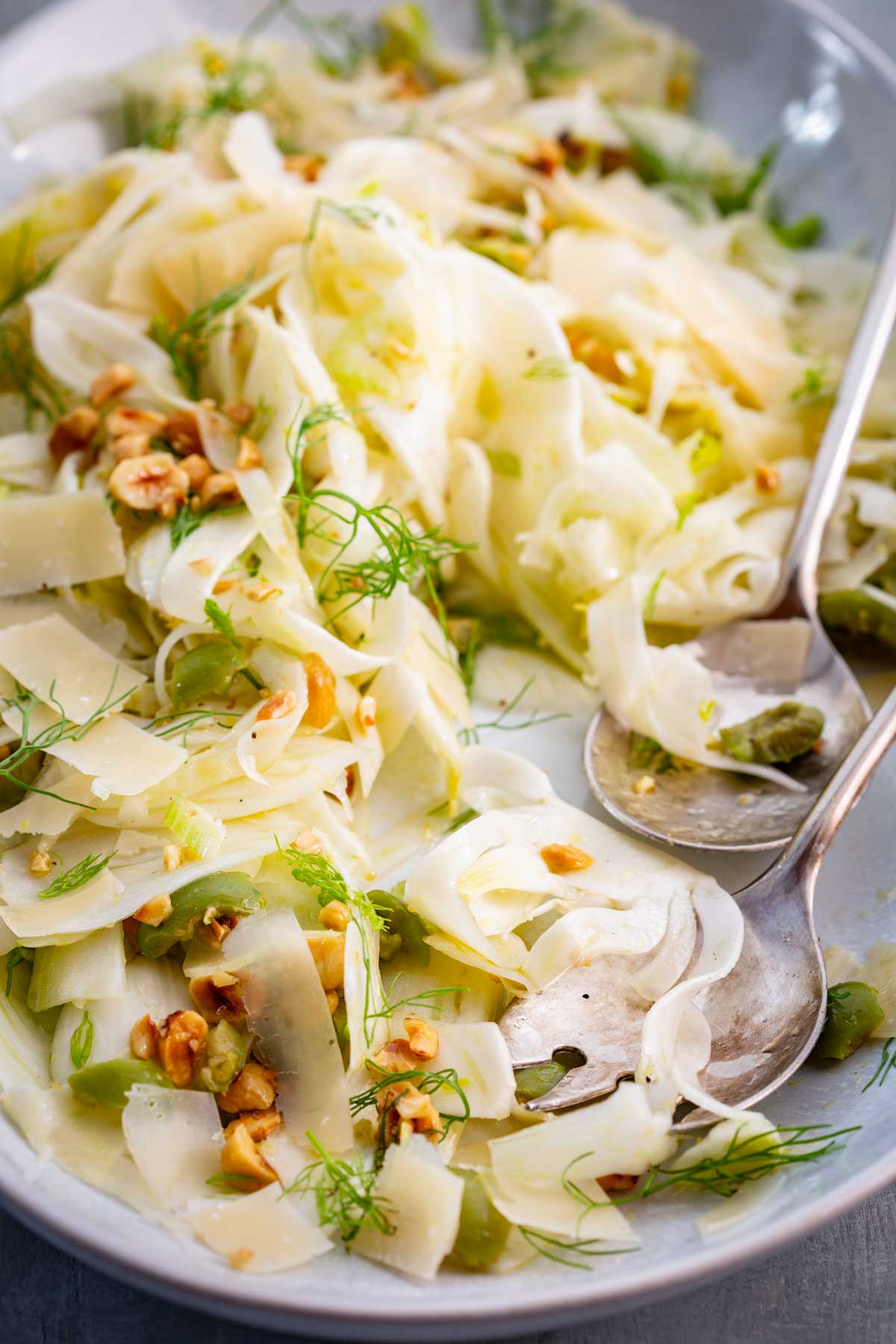 Side view of shaved fennel salad in a serving plate with serving spoons.