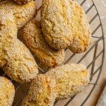 Close-up overhead shot of Italian sesame seed cookies stacked on a round wire cooling rack, showing their oval shape and dense coating of toasted sesame seeds with a golden-baked exterior.