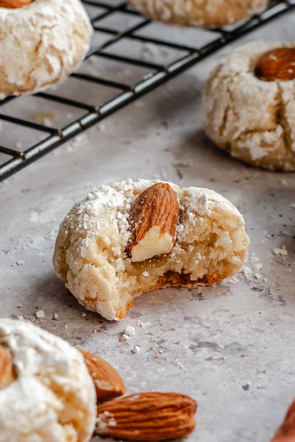 Italian almond cookie with a bite taken out next to more cookies and a cookie tray.