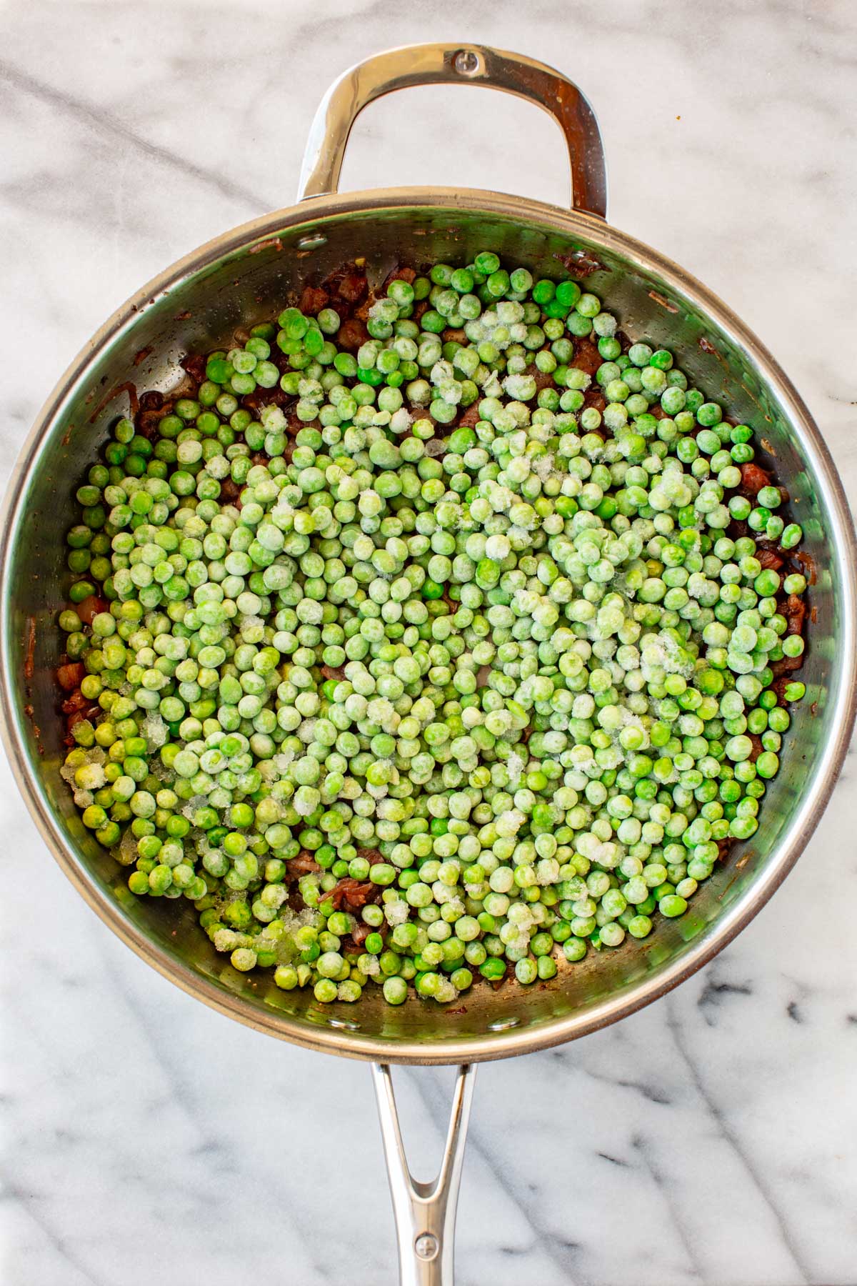 Frozen green peas poured over the pancetta and shallot mixture in a stainless steel skillet.