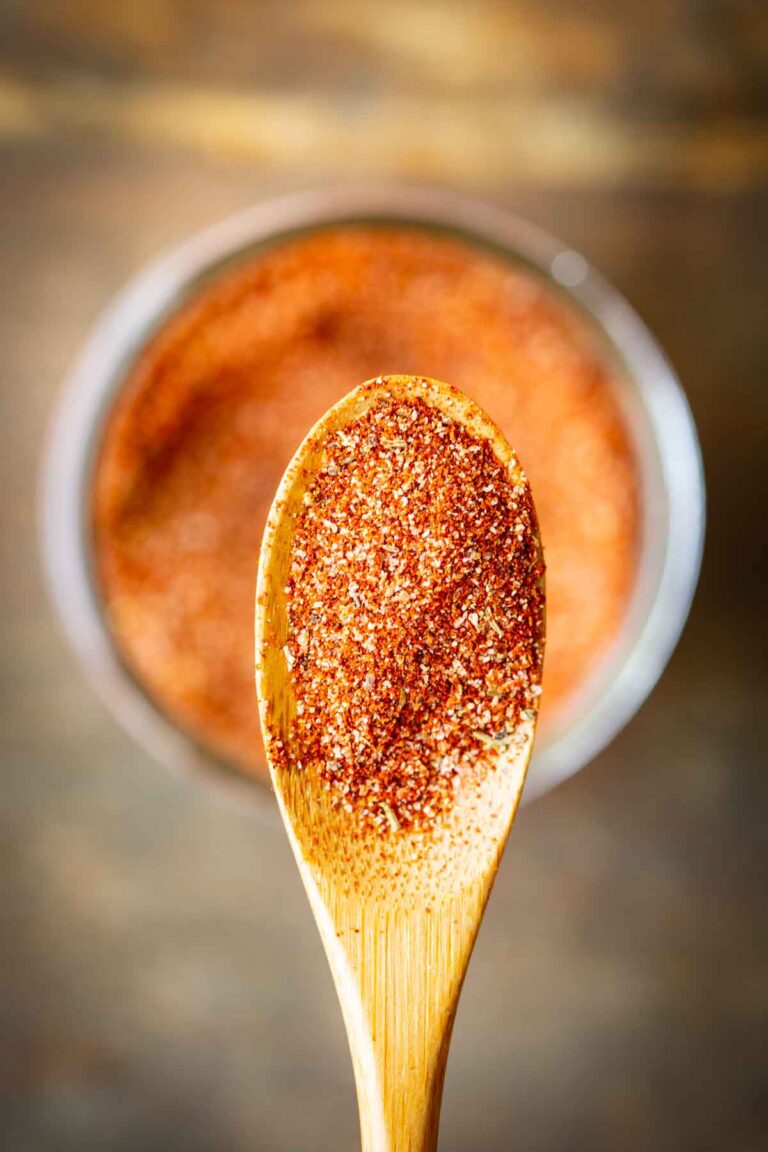 Close-up shot of a wooden spoon piled with blackening seasoning, with the filled jar blurred in the background.