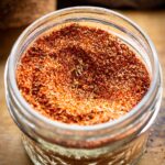 Overhead close-up of a glass jar filled with blackening seasoning, showing the texture of the paprika, herbs, and spices.