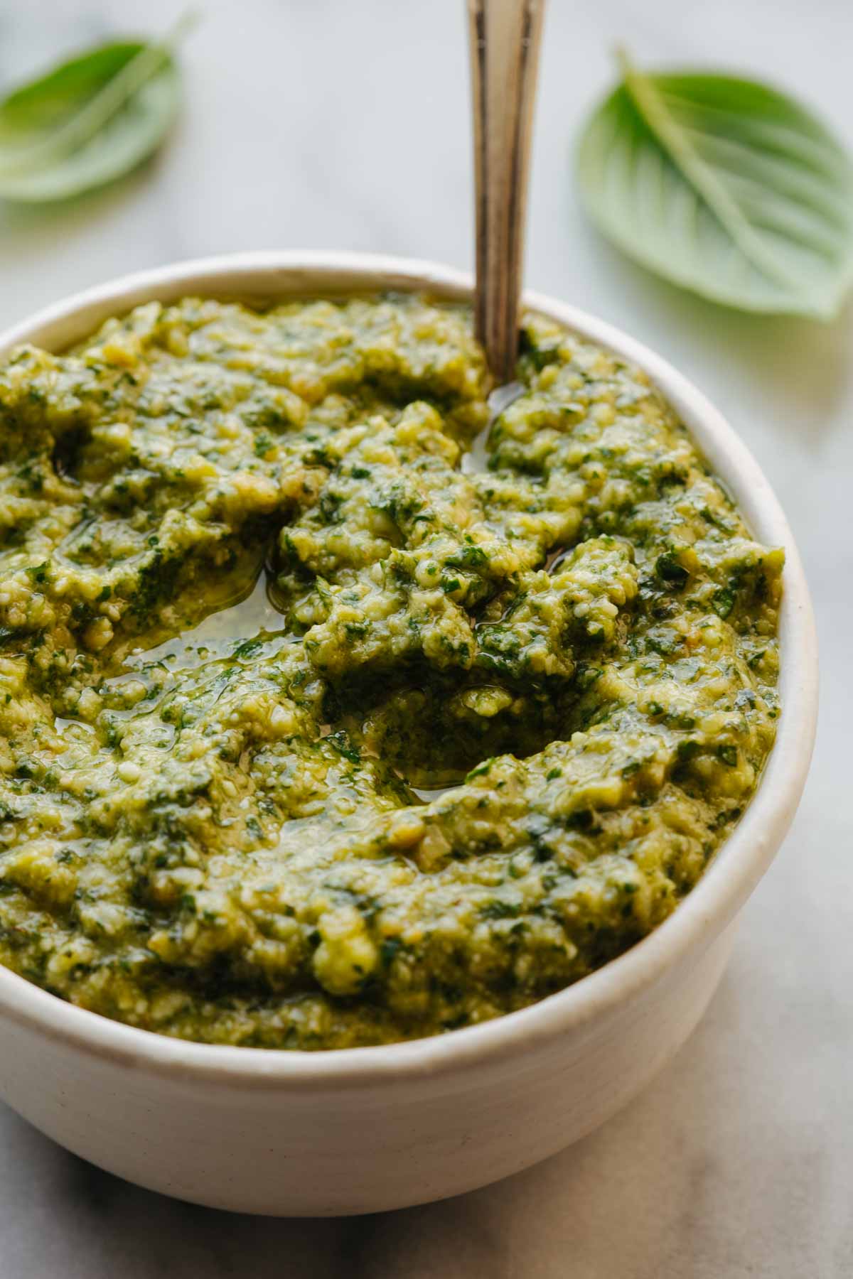 Close-up shot of long hot pepper pesto in a white bowl, showing the pesto's texture with visible olive oil pooling on top.
