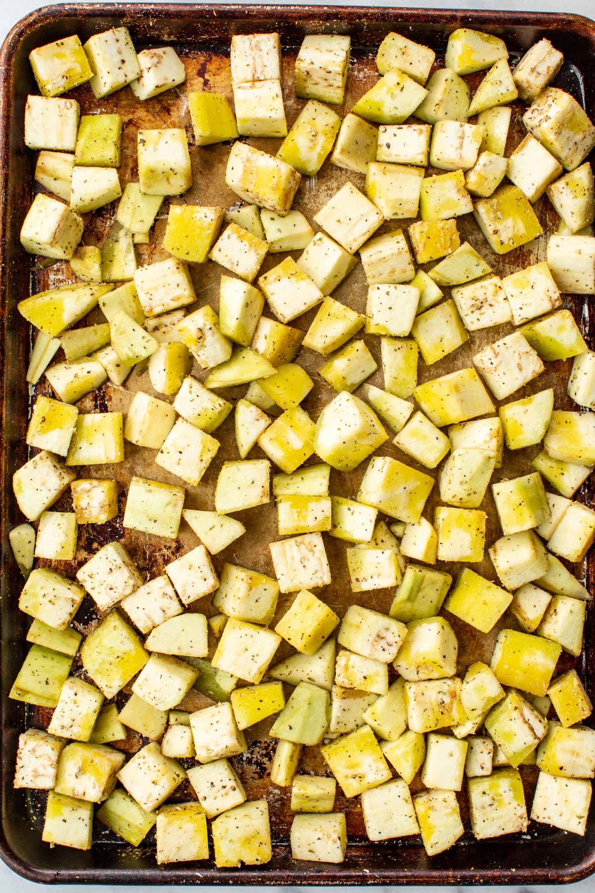 Cubed eggplant with oregano and garlic powder spread on a baking sheet.