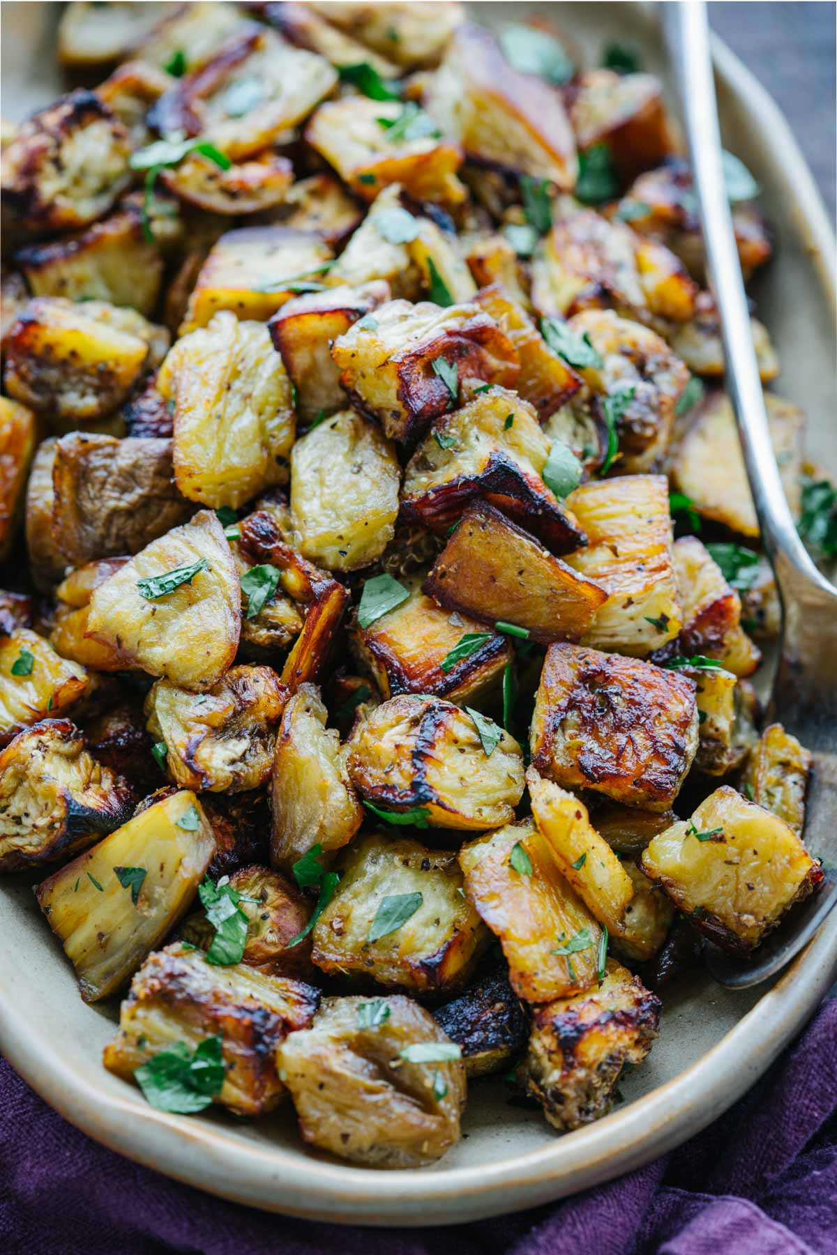 Roasted eggplant with crispy caramelized edges on a platter with a serving spoon.